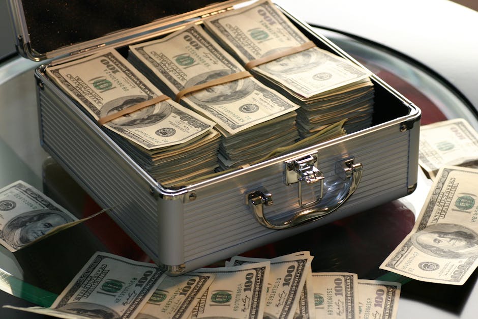 Open briefcase filled with stacks of hundred dollar bills on a glass table, representing wealth